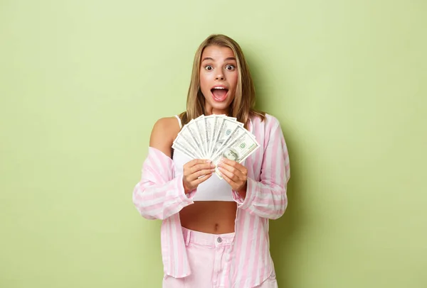 Immagine di una ragazza eccitata che vince il premio, con denaro in mano e sorridente sorpresa, in piedi su sfondo verde — Foto Stock