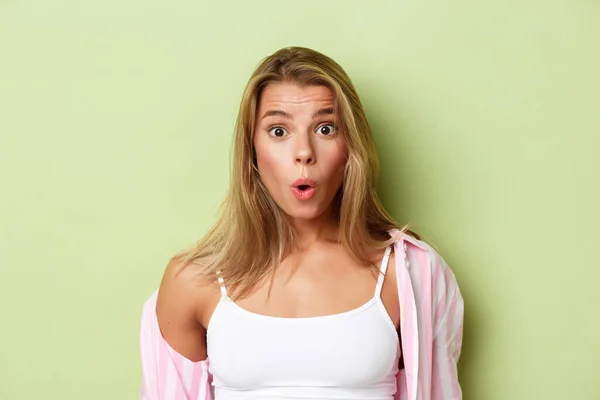 Close-up van aantrekkelijke blonde vrouw in roze shirt, kijken verrast, zeggen wow gefascineerd, staande over groene achtergrond — Stockfoto