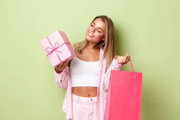 穿着时髦的金发女孩度假购物的画像，手持礼品盒和粉红包，站在绿色的背景上 — 图库照片