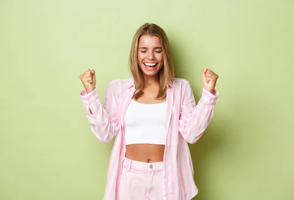 Портрет успешной современной деловой женщины в розовой рубашке, делающей кулачный насос приятным и говорящим "да", улыбающейся довольной, торжествующей от радости и победы, стоящей на зеленом фоне — стоковое фото