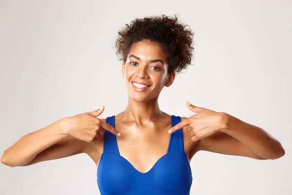 Närbild av leende afrikansk-amerikansk flicka idrottsman, pekar finger på mitten, visar din logotyp om träning eller sport, står mot vit bakgrund — Stockfoto