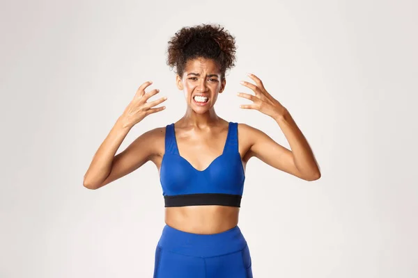 Concept van sport en training. Taille-up van gefrustreerde jonge Afrikaans-Amerikaanse fitness vrouw in blauw uniform, handen schudden en grimmig, op zoek gefrustreerde, witte achtergrond — Stockfoto