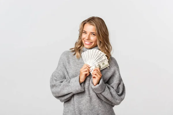 Afbeelding van mooi blond meisje in grijze trui, met geld en glimlachen, denken hoe om geld te verspillen, witte achtergrond — Stockfoto