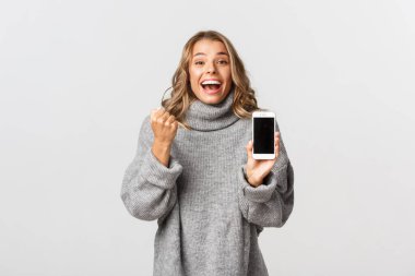 Mutlu sarışın bir kızı kazanmanın, online başarıyı yenmenin, akıllı telefon ekranını göstermenin ve yumruk pompası yapmanın, beyaz arka plan