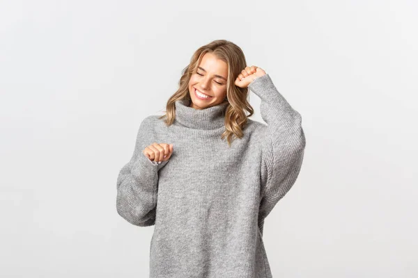 Primer plano de la atractiva chica rubia, vistiendo suéter gris, bailando y sonriendo feliz, de pie sobre fondo blanco —  Fotos de Stock