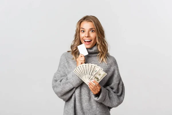 Studio shot van opgewonden aantrekkelijke meisje met geld en creditcard, glimlachen op camera, staande over witte achtergrond — Stockfoto