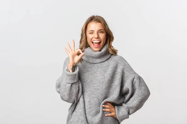 Mujer sonriente de confianza que no muestra ningún gesto de problema, hacer signo de bien y guiño seguro de sí mismo, de pie sobre el fondo blanco —  Fotos de Stock