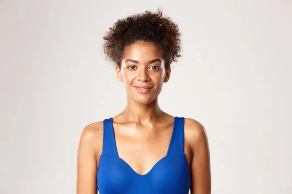 Concepto de entrenamiento y deporte. Primer plano de atractiva mujer fitness sonriente en sujetador deportivo azul, mirando feliz, de pie sobre fondo blanco — Foto de Stock