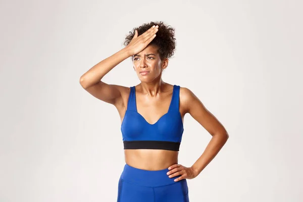 Studio skott av besviken afrikansk-amerikansk fitness kvinna i blå sport oufit, slå hennes panna och grimma, står mot vit bakgrund — Stockfoto
