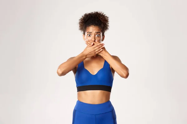Midjan upp av rädd och chockad afrikansk-amerikansk kvinnlig idrottsman, stänga munnen med händerna, hålla skrik, står mot vit bakgrund — Stockfoto