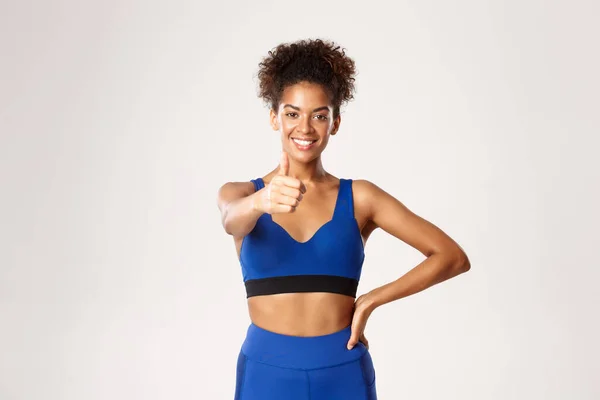 Gezond en fit Afrikaans-Amerikaanse sportvrouw, met duimen omhoog in goedkeuring, adviseren sportschool of workout app, staan tegen een witte achtergrond — Stockfoto