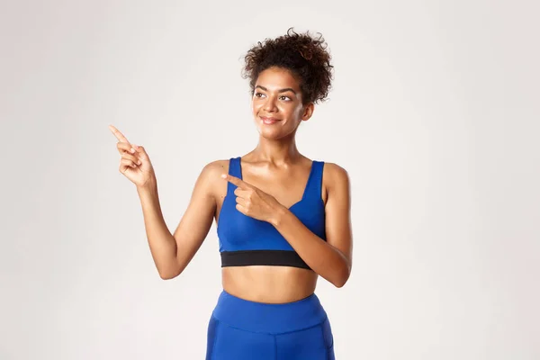 Studio shot van gezonde en fit Afrikaans-Amerikaanse vrouwelijke atleet, wijzen en kijken links met een vrolijke glimlach, staande over een witte achtergrond — Stockfoto