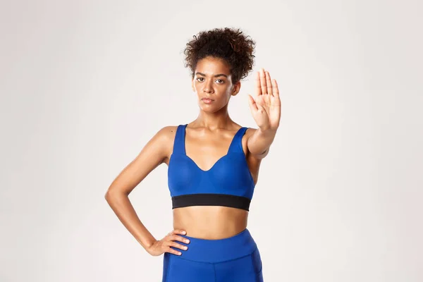 Midjan upp av allvarliga afrikansk-amerikanska fitness kvinna, idrottsman visar stopp gest, förbjuda något dåligt, står i blå sport outfit över vit bakgrund — Stockfoto