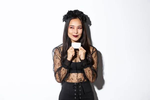 Siyahi gotik elbiseli düşünceli Asyalı kadının bir planı var, kredi kartı tutuyor, sol üst köşeden gülümsüyor. — Stok fotoğraf