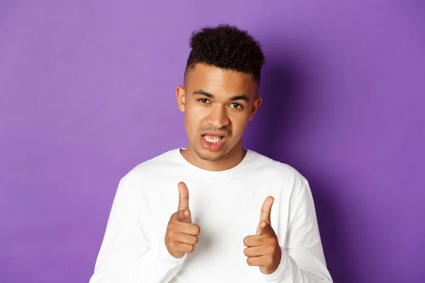 Close-up of cool and sassy african-american guy, pointing fingers at camera, praising good job, congratulate you, standing over purple background — Stock Photo, Image