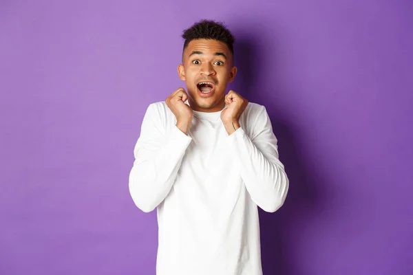 Retrato de chico afroamericano asombrado en camisa casual blanca, boca abierta fascinado y mirando promoción fresco, de pie sobre fondo púrpura —  Fotos de Stock