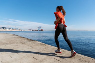 Aktif ve sağlıklı bir kadın kıyı şeridi boyunca koşuyor. Deniz kenarında spor yapan kadın.