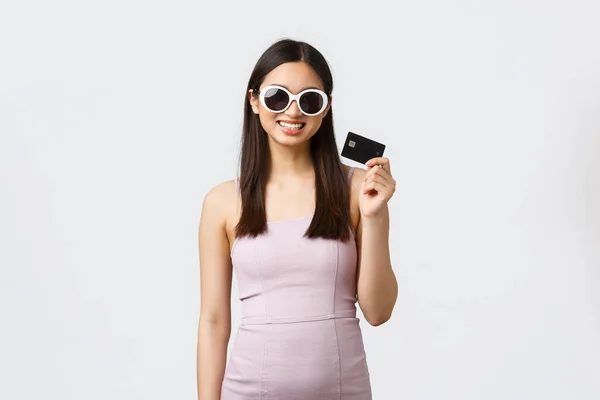 Stile di vita, shopping e turismo. Splendida donna asiatica in abito e occhiali da sole vantarsi con nuova carta di credito piena di soldi, pronti a comprare nuovi vestiti per le vacanze estive, sorridente soddisfatto — Foto Stock