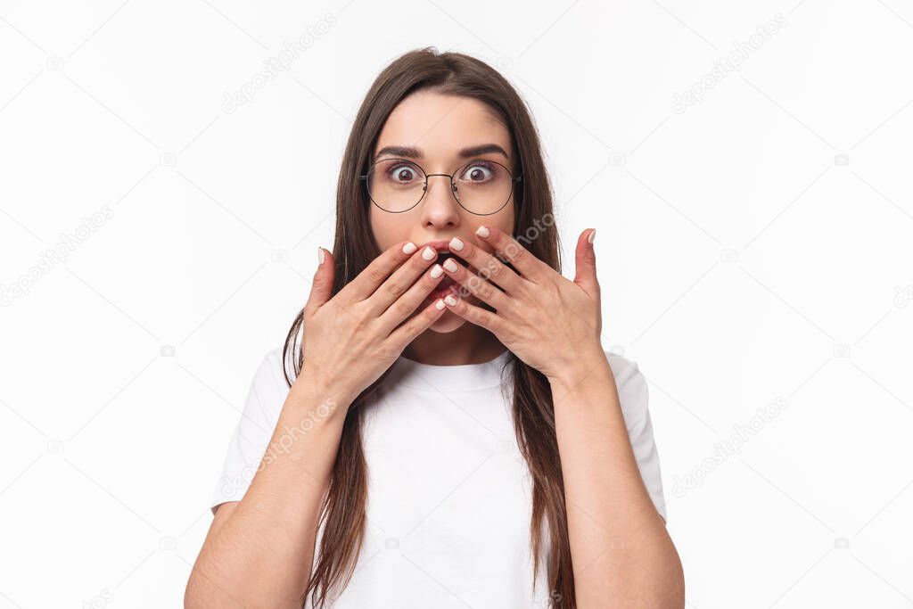 Close-up portrait of enthusiastic, shocked and amazed young happy girl hear awesome gossip, spilled tea, cover opened mouth with palms, express surprise with eyes, white background