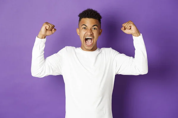 Imagen de un chico afroamericano animado, gritando y mirando determinado, ganando algo, logrando gol y celebrando la victoria, de pie sobre fondo púrpura —  Fotos de Stock