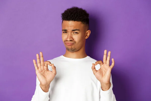 Imagem do homem afro-americano satisfeito em camisola branca, elogiar algo bom, mostrando sinais ok e aceno de aprovação, de pé sobre fundo roxo — Fotografia de Stock