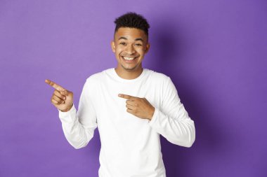 Beyaz kazaklı yakışıklı Afro-Amerikan 20 'li yaşlardaki bir adamın resmi. Parmaklarını solu gösteriyor ve gülümsüyor. Fotokopi alanında müthiş bir tanıtım ya da logo gösteriyor.