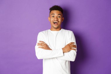 Beyaz kazaklı, yakışıklı, Afro-Amerikan bir adamın resmi, ağzı açık ve şaşırmış görünüyor, senin logon için mor fotokopi alanının yanında duruyor.