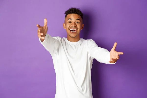 Portrét šťastného a vzrušeného afroamerického mladíka, který se natahuje, aby něco uchopil, natahuje ruce k objetí a usmívá se, stojí nad fialovým pozadím — Stock fotografie