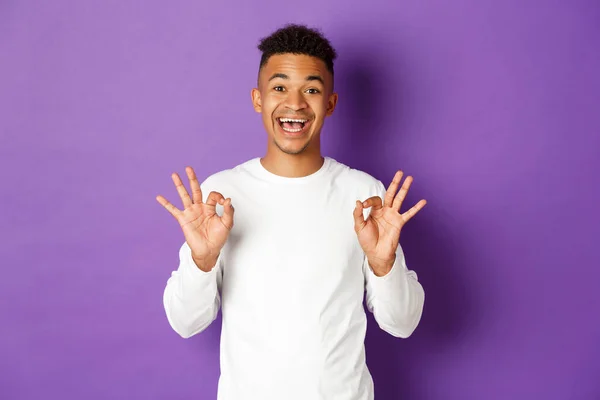 Image of satisfied african-american guy showing okay signs, being pleased with something, like and approve, standing over purple background — Stock Photo, Image