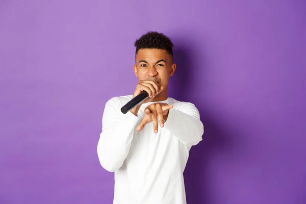 Obrázek drzého afroameričana, jak zpívá v mikrofonu, klepe a ukazuje na kameru, stojí nad fialovým pozadím — Stock fotografie