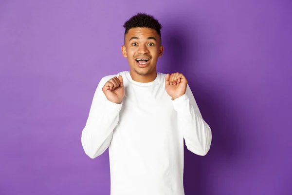 Imagen del hombre afroamericano esperanzado, mirando con anticipación a la cámara, sonriendo y saltando de la emoción, de pie sobre el fondo púrpura —  Fotos de Stock