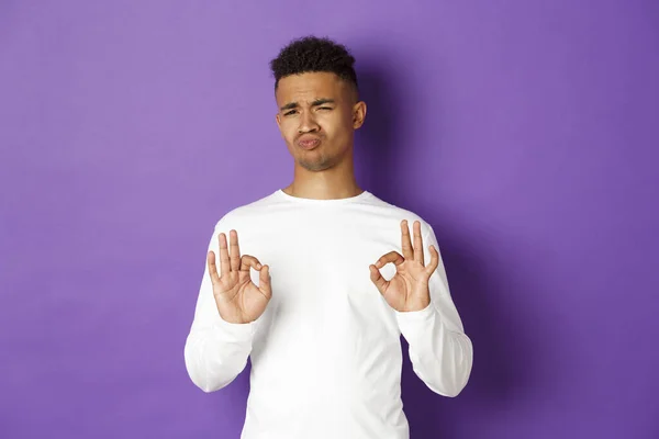 Satisfeito homem afro-americano bonito, mostrando sinais ok e olhando impressionado, louvar algo bom, de pé sobre fundo roxo — Fotografia de Stock