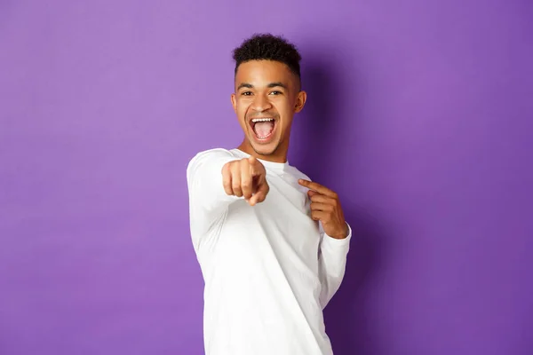 Ritratto di uomo afro-americano allegro in felpa bianca, che sceglie te, punta il dito contro la macchina fotografica per congratularsi con qualcosa, in piedi su sfondo viola — Foto Stock