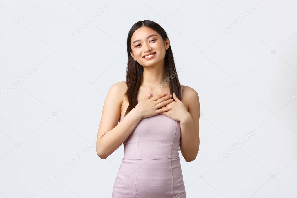 Celebration, beauty and glamour concept. Smiling pleased and happy asian woman in stylish party dress, touch heart in appreciation, receive praises and compliments, looking flattered
