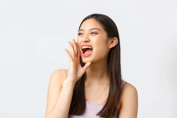 Belleza, moda y gente concepto de emociones. primer plano retrato de despreocupado feliz asiático chica haciendo ruidoso anuncio, sosteniendo la mano cerca de abierto boca como gritando, blanco fondo — Foto de Stock