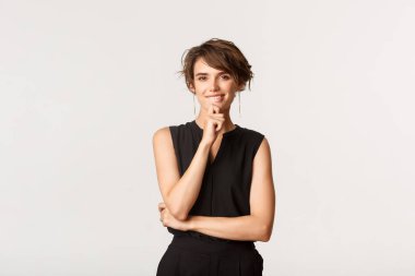 Yaratıcı, zarif, gülümseyen genç bir kadının portresi. Kameraya düşünceli bakıyor, beyaz arka plan üzerinde düşünüyor.