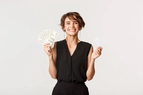 Gelukkig succesvolle vrouw glimlachen, tonen credit card en geld, staande over witte achtergrond — Stockfoto