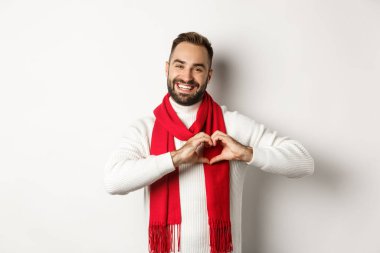 Noel tatili ve yeni yıl konsepti. Mutlu baba kalp işareti gösteriyor ve gülümsüyor, seni seviyorum jest, kışlık süveter ve eşarp, beyaz arka plan