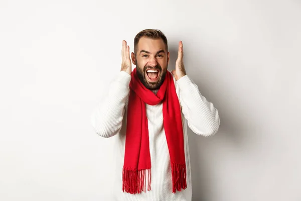 Weihnachtsurlaub und Neujahrskonzept. Wütender Mann schreit und schreit, schüttelt Hände in Kopfnähe mit frustriertem Gesichtsausdruck, steht vor weißem Hintergrund — Stockfoto