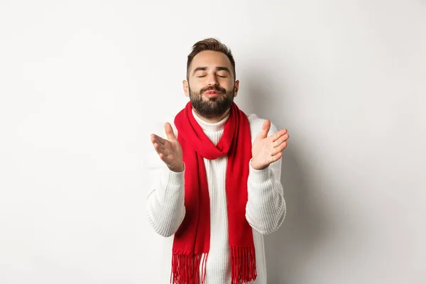 Schöner Mann im Weihnachtspulli mit geschlossenen Augen, aufgerissenen Lippen, zum Küssen angelehnt, vor weißem Hintergrund stehend — Stockfoto