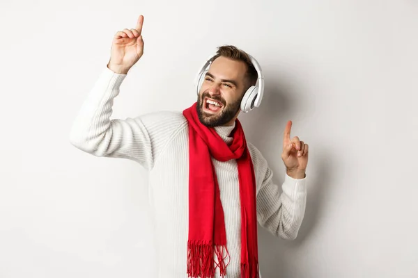 Wintervakantie en technologie concept. Happy man dansen op muziek in hoofdtelefoon, staande over witte achtergrond in trui — Stockfoto