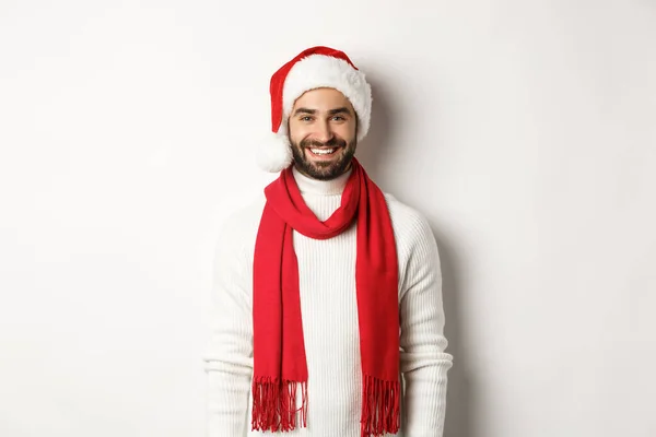 Weihnachtsferien. Lächelnder bärtiger Mann mit Weihnachtsmütze und rotem Schal, glücklich lächelnd, vor weißem Hintergrund stehend — Stockfoto