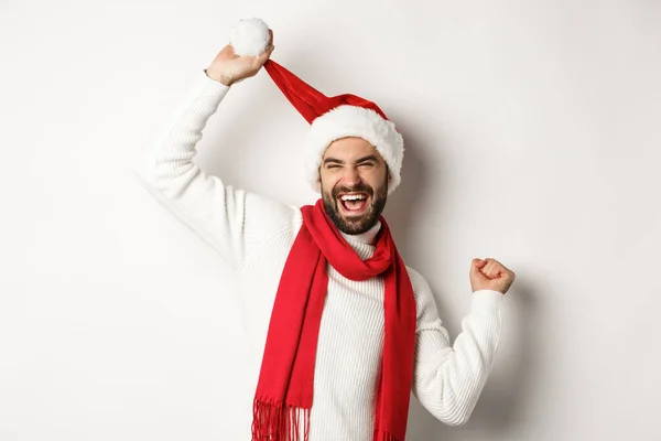 Winterurlaub und Neujahrsparty. Glücklicher Mann mit Weihnachtsmütze und rotem Schal, der vor weißem Hintergrund tanzt — Stockfoto