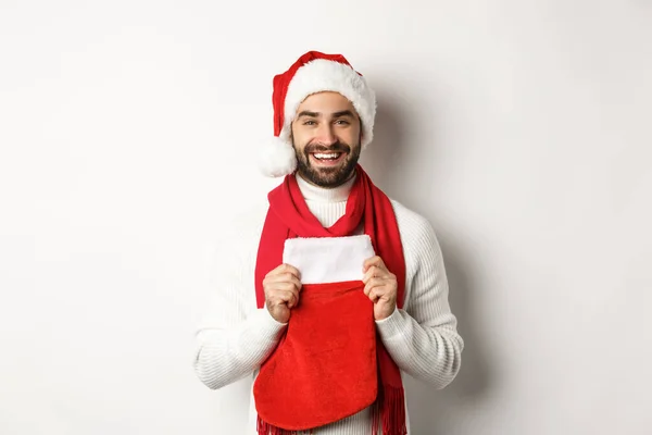 Kış tatili ve alışveriş konsepti. Yakışıklı sakallı adam Noel çorabında hediyeler getiriyor, gülümsüyor ve mutlu yıllar diliyor, beyaz bir geçmişi var. — Stok fotoğraf