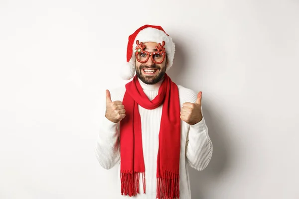 크리스마스, 새해, 축하하기. 산타 모자와 당원용 안경을 쓴 흥분 한 남자, 승인하여 엄지손가락을 들고 만족 스러운 하얀 배경을 웃으며 — 스톡 사진