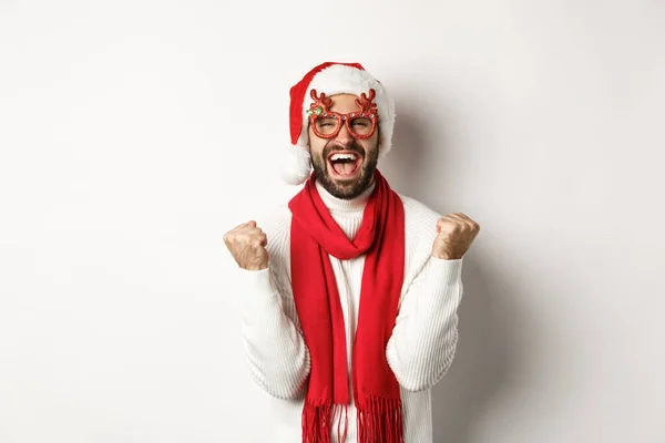 Natal, Ano Novo e conceito de celebração. Homem animado em chapéu de Papai Noel e óculos de festa, ganhando e se alegrando, fazendo bomba punho, gritando sim, de pé sobre fundo branco — Fotografia de Stock