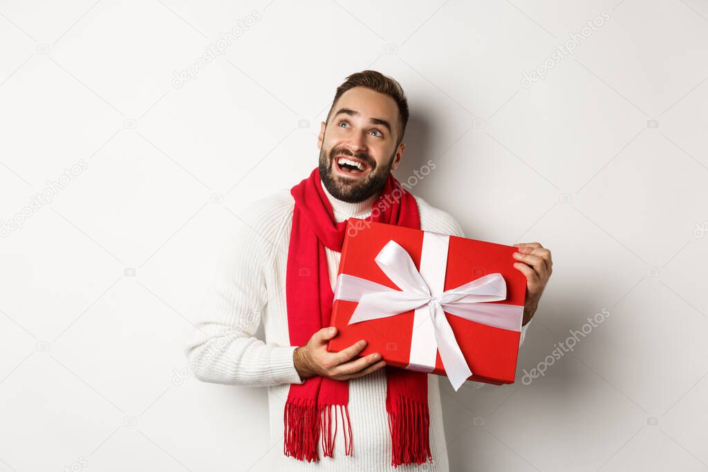 Merry Christmas. Happy man looking ecstatic and holding his New Year gift, standing against white background