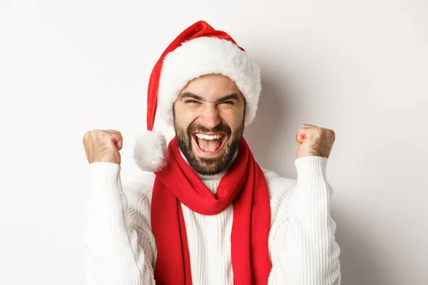 Neujahrsparty und Winterferienkonzept. Großaufnahme eines aufgeregten Mannes mit Weihnachtsmütze, der jubelt, gewinnt oder mit Weihnachtsmütze feiert, vor weißem Hintergrund — Stockfoto