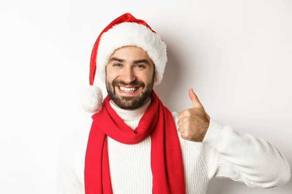 Festa de Ano Novo e conceito de férias de inverno. Close-up de homem feliz em chapéu de Papai Noel mostrando polegares para cima em aprovação, como e concordar, de pé sobre fundo branco — Fotografia de Stock