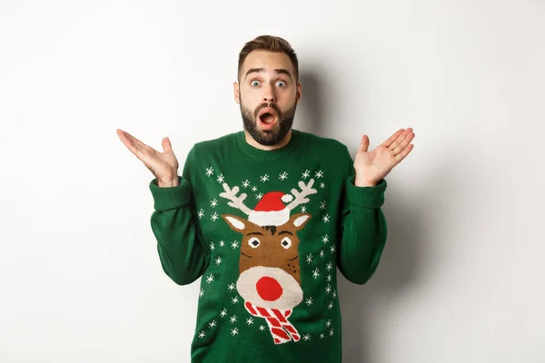 Fiesta de Año Nuevo y concepto de vacaciones de invierno. Sorprendido barbudo jadeando sorprendido, de pie en suéter de Navidad, fondo blanco — Foto de Stock